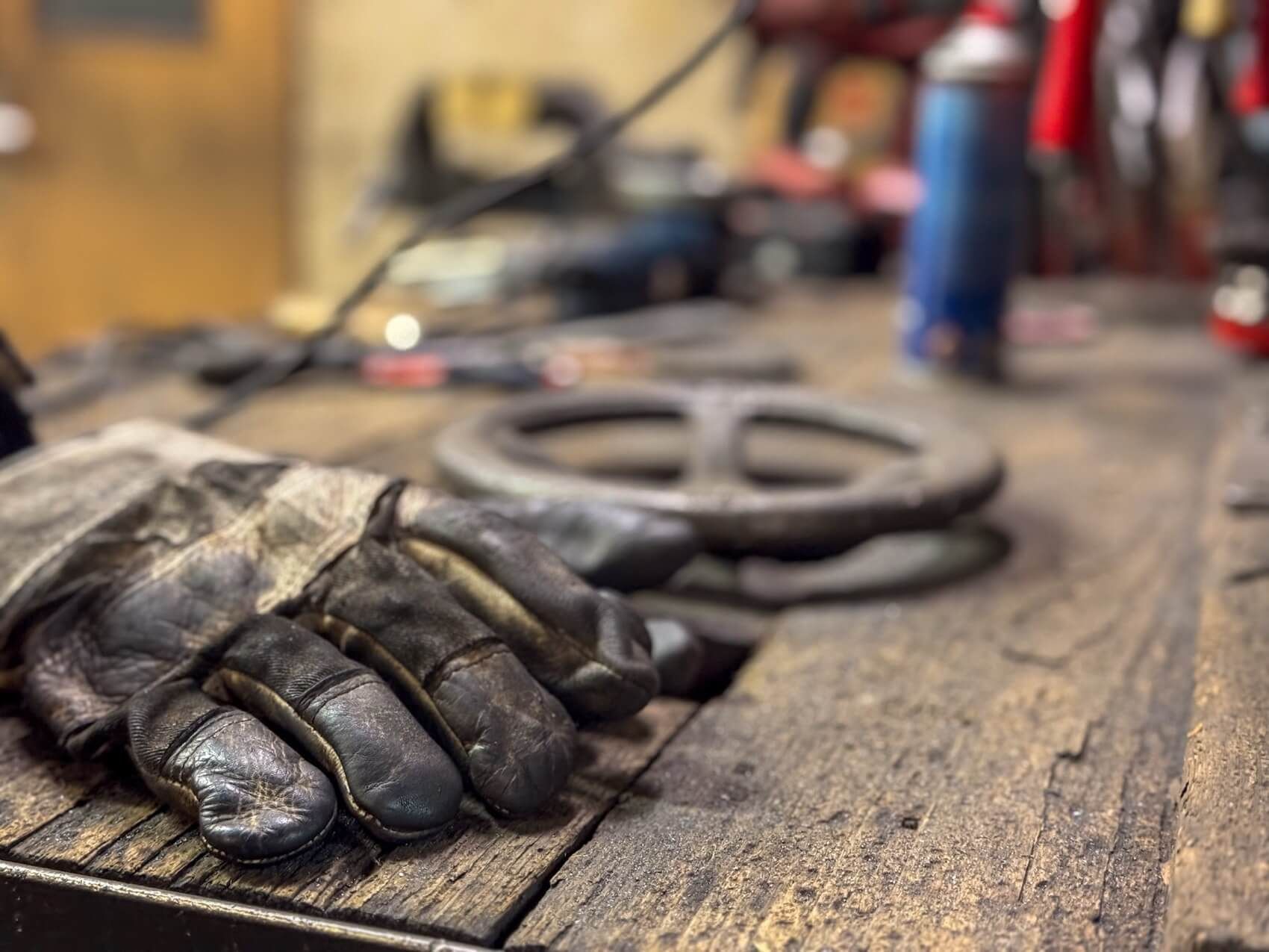 Blick auf eine Werkbank mit Schweißhandschuh im Vordergrund und Tiefenschärfe  
